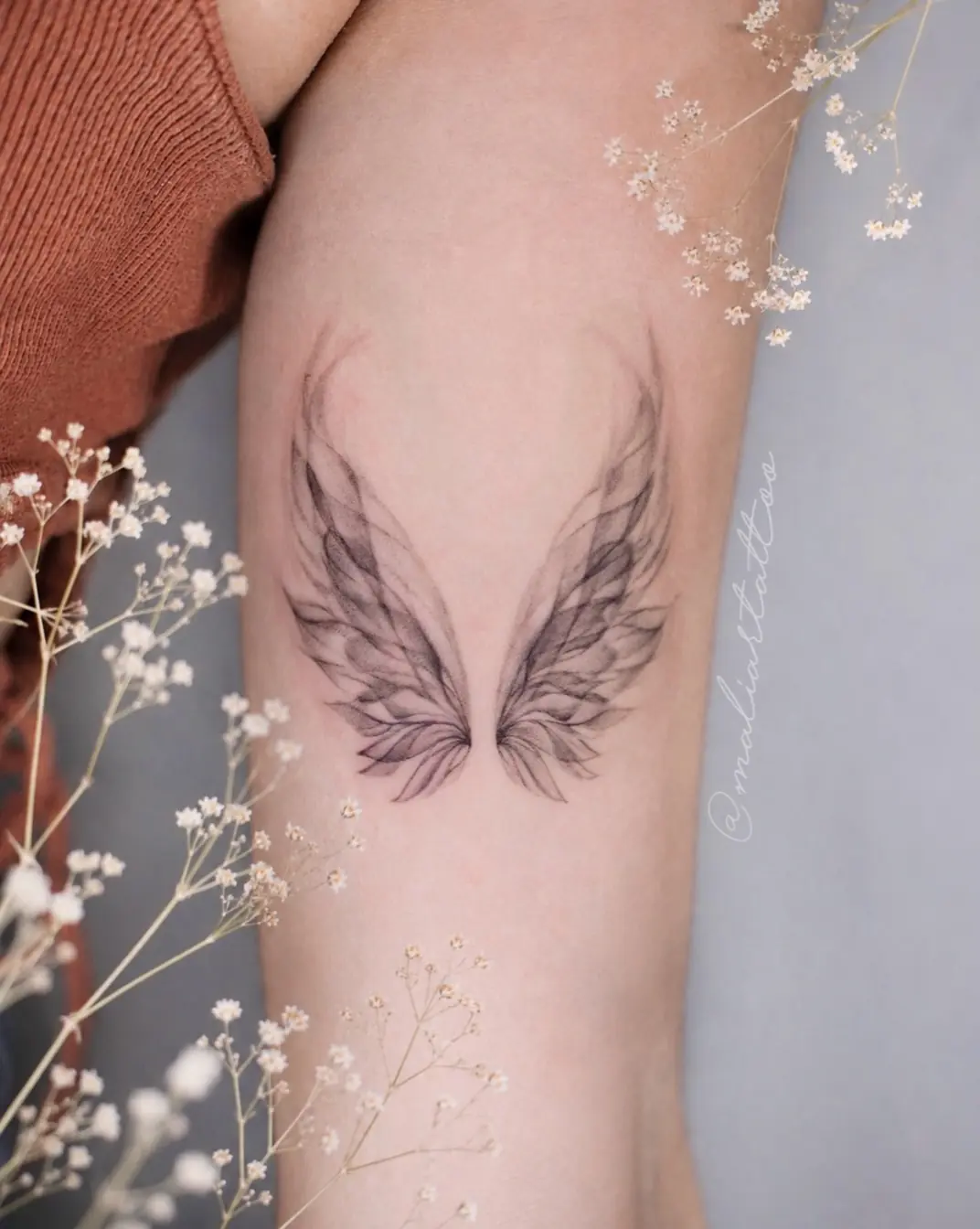 Alas, tatuaje de línea fina, humo y transparencias en brazo